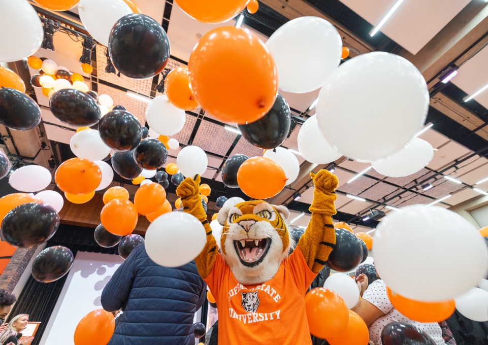 Benji stands in a shower of orange, black, and white balloons